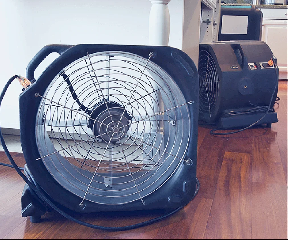 Professional air movers and drying equipment running on a hardwood floor